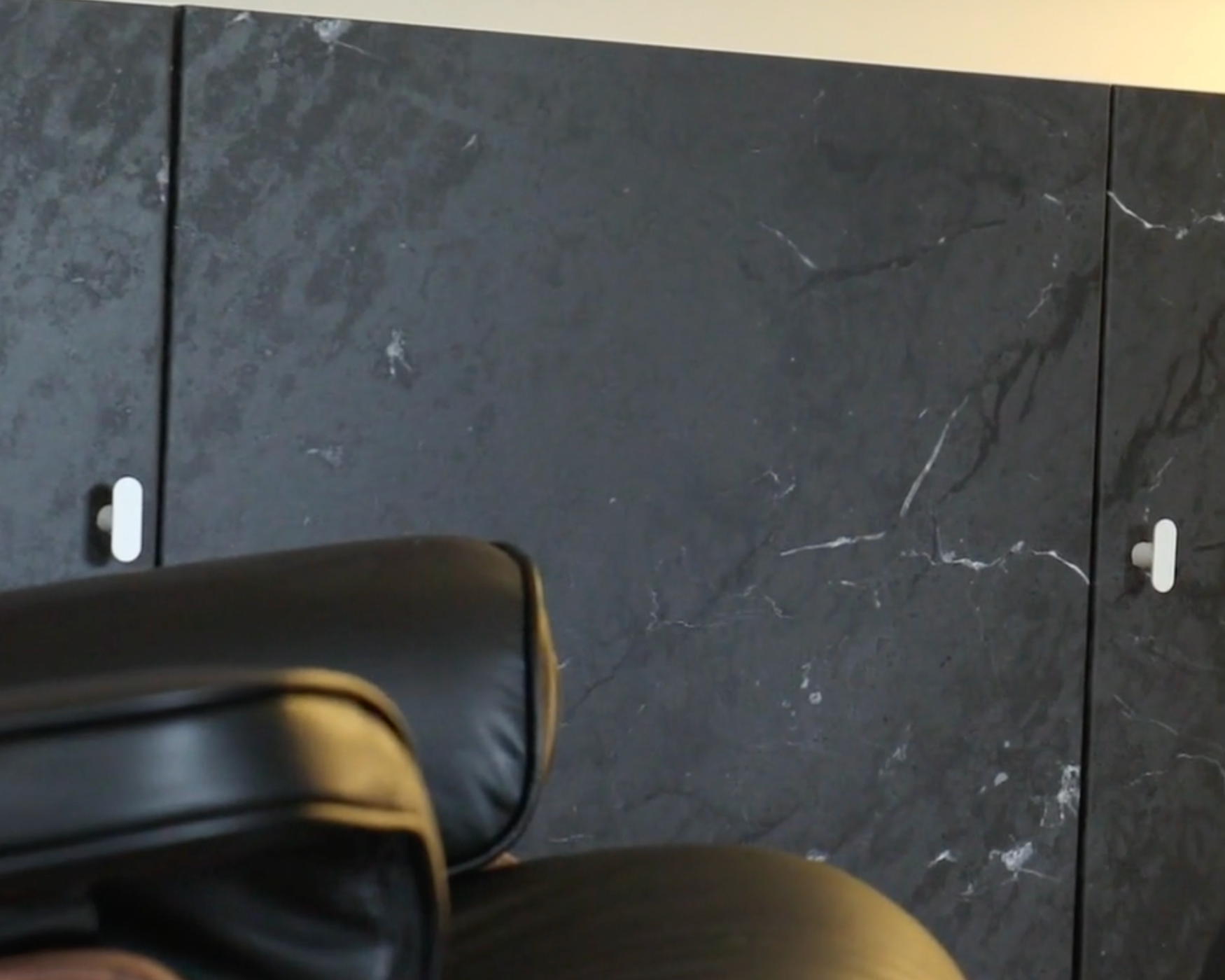 Black marble cabinet with white t-bar knobs, paired with sleek black leather seating for a bold, edgy interior look.