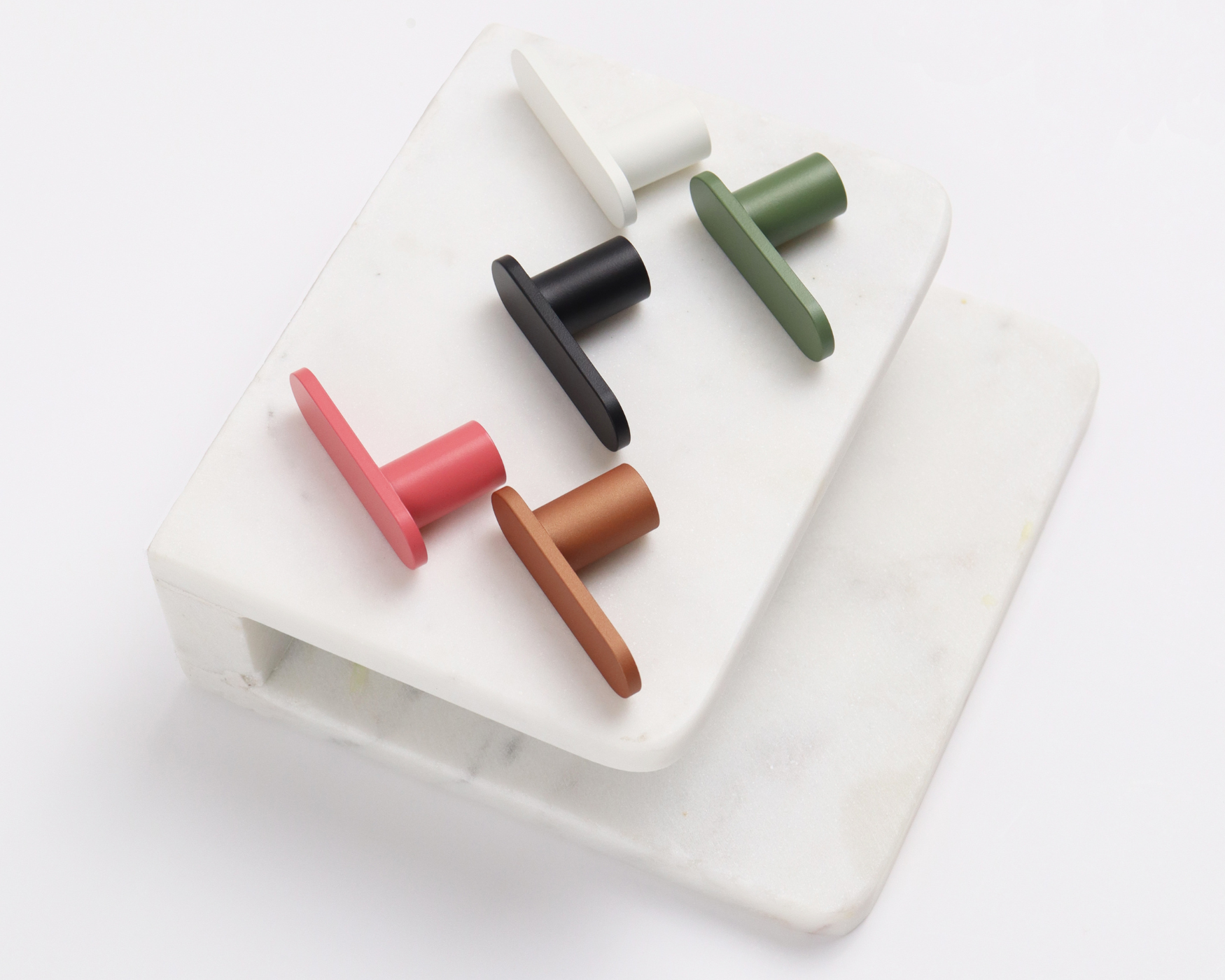 Assorted T-bar cabinet knobs in various colors: white, black, green, pink, and copper, displayed on a white marble surface.