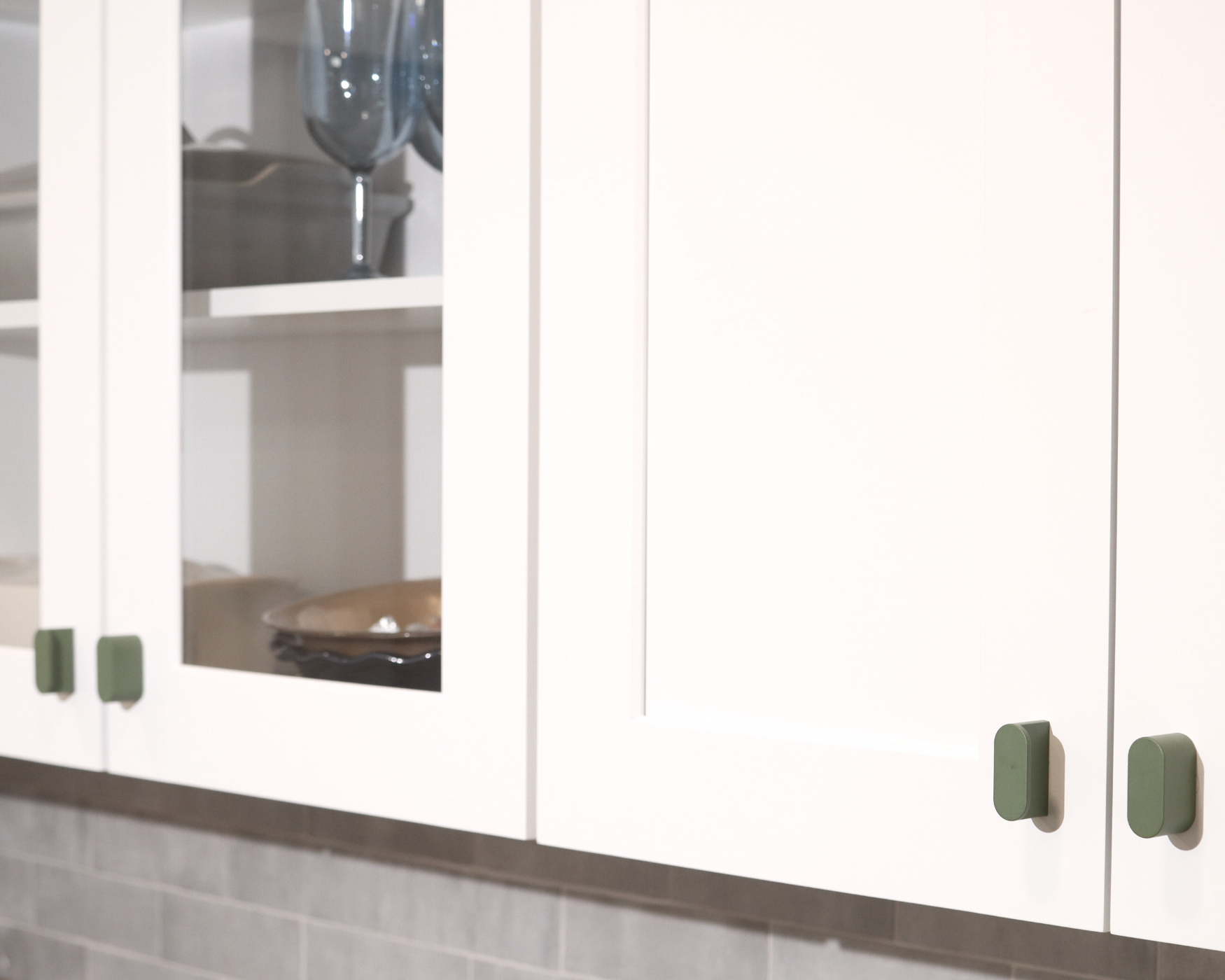 White kitchen cabinets with glass doors and green olive-colored knobs, adding a modern touch of color and style to the design