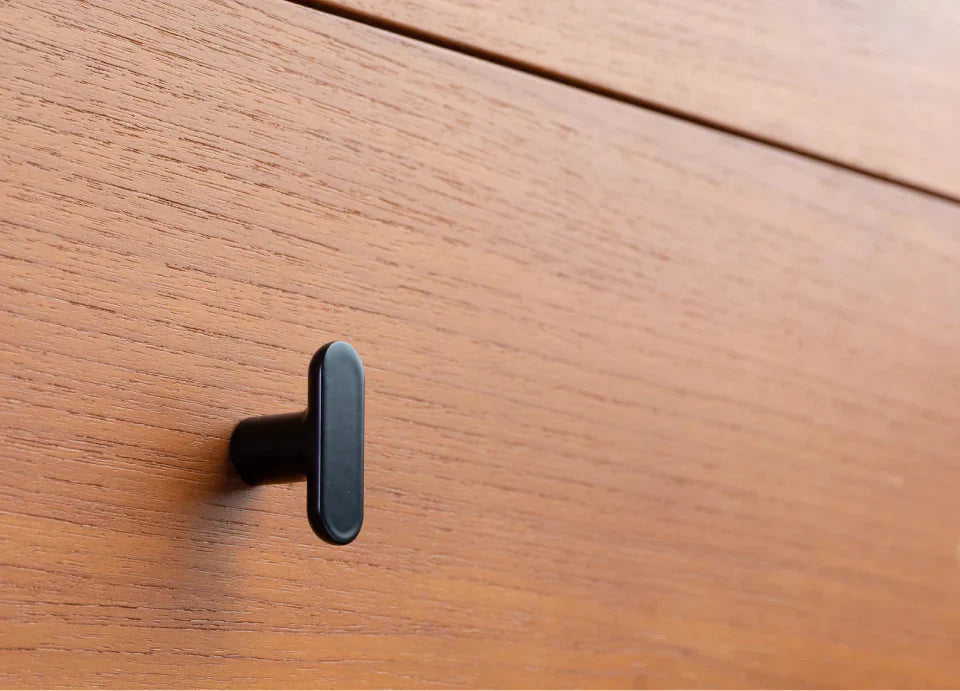 Matte black T-bar cabinet knob on a warm wood drawer, showcasing mid-century modern design with minimalist flair.
