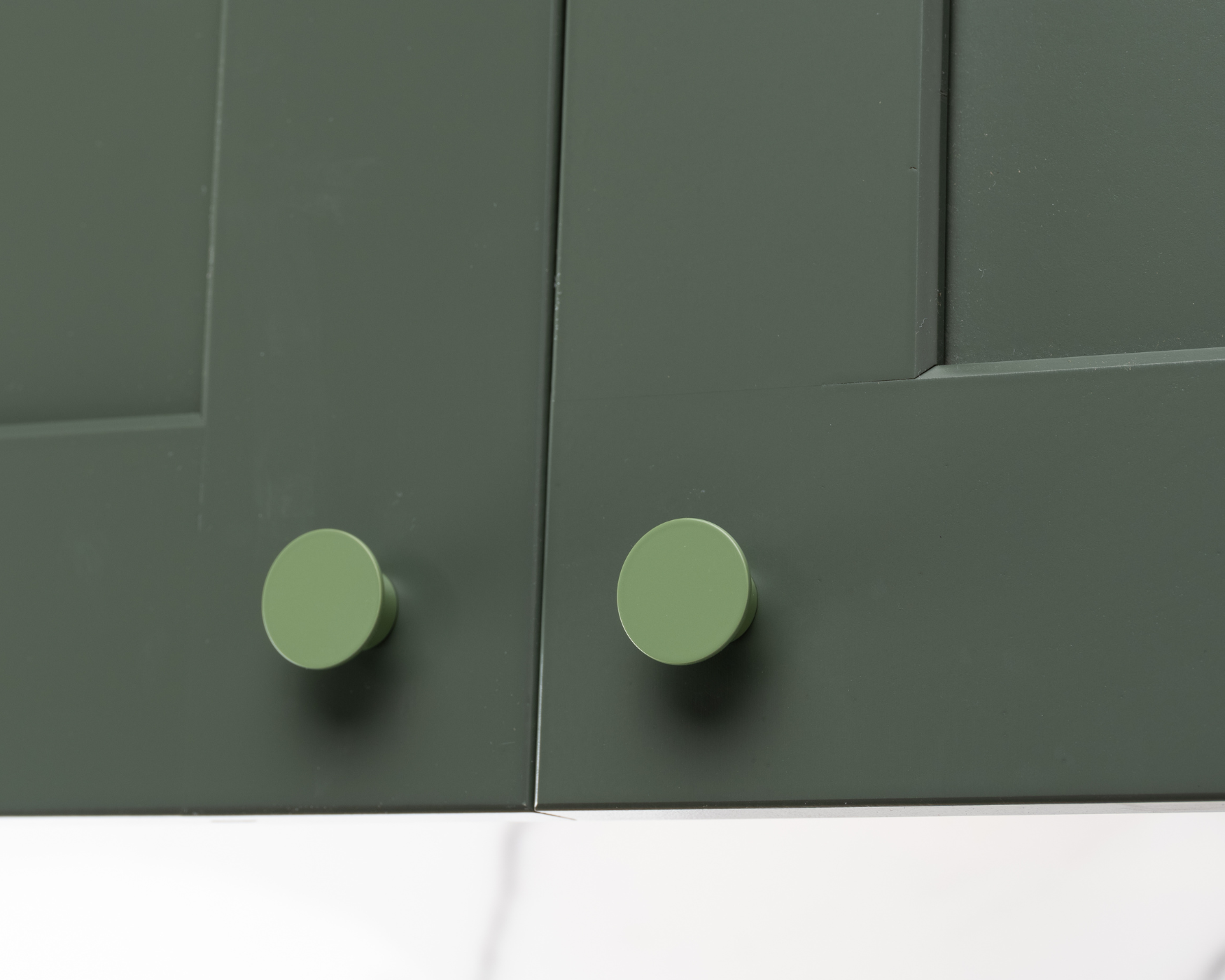 Green cabinet knobs with a smooth, round design, adding a touch of sophistication and warmth to this kitchen's olive-themed look.