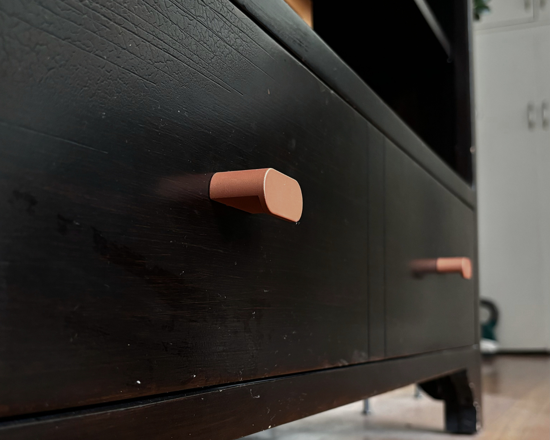 Close-up of a black TV stand upgraded with modern copper oval knobs, showcasing stylish ROUS hardware.