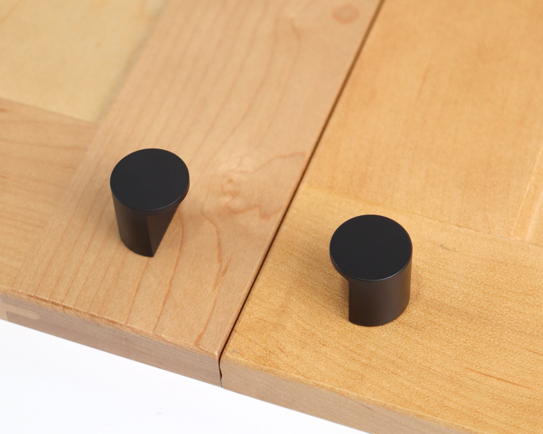 Matte black cutout knobs with a tapered base mounted on light wood cabinet doors, offering a sleek modern hardware contrast.