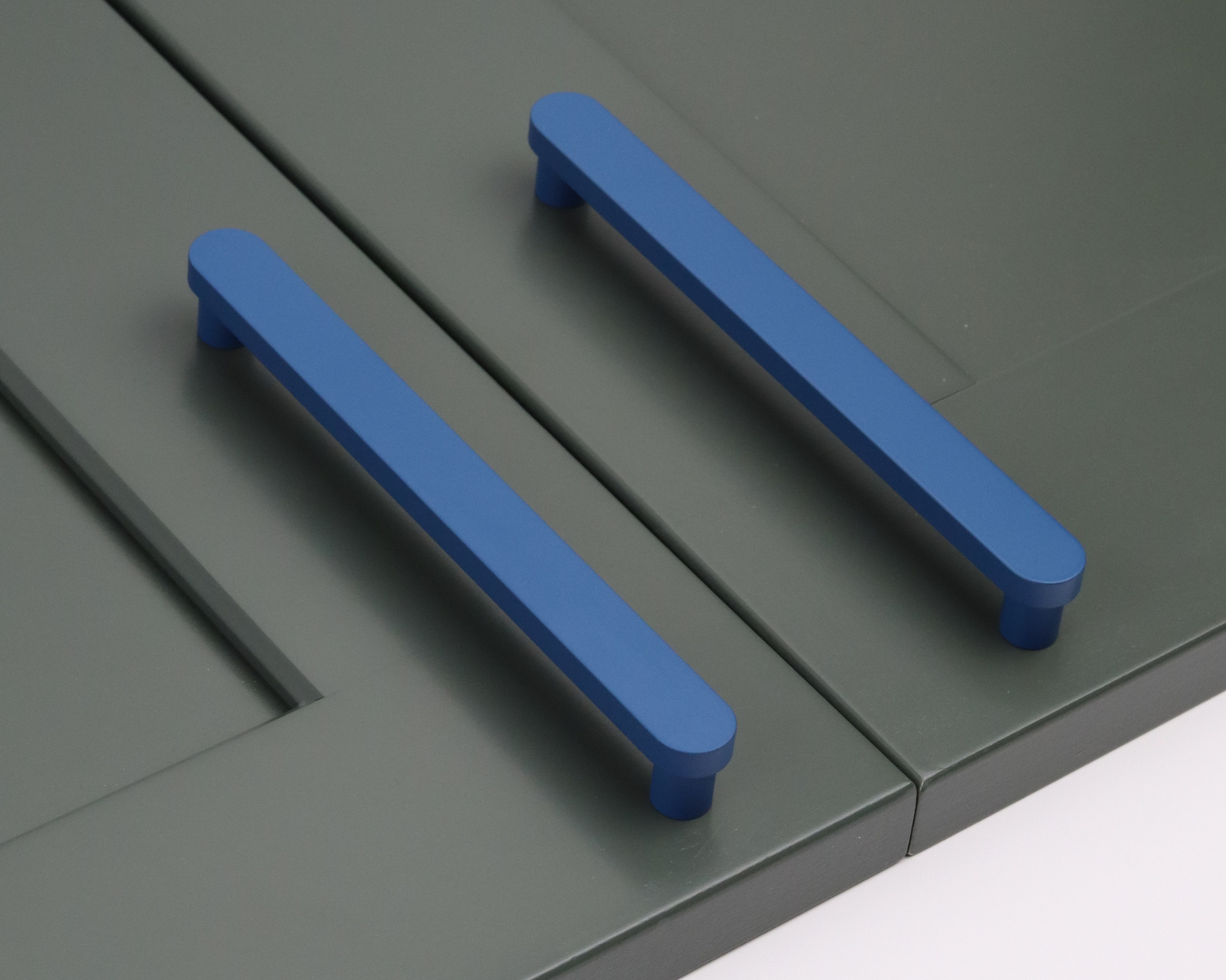 Matte navy blue T-bar cabinet pulls mounted on sage green shaker-style cabinet doors, showcasing modern hardware styling.