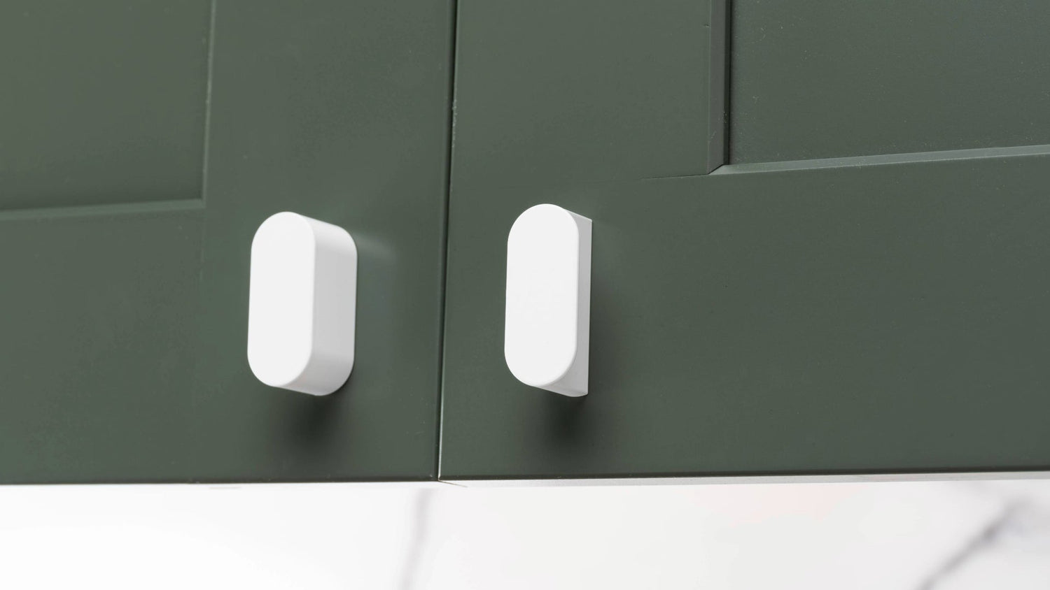 Close-up of modern kitchen cabinet doors with sleek white Oval knobs, demonstrating precise and ergonomic hardware placement.