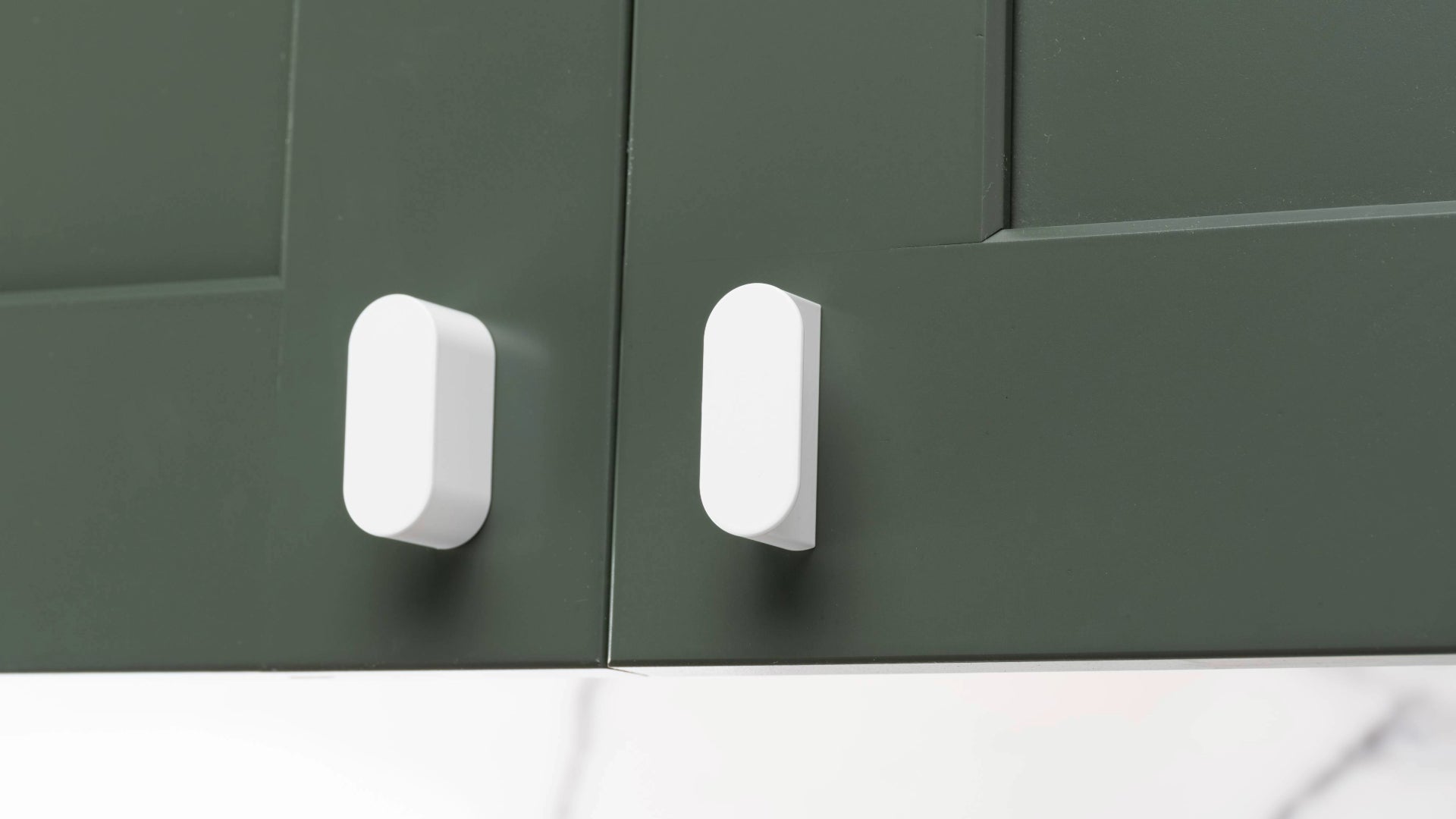 Close-up of modern kitchen cabinet doors with sleek white Oval knobs, demonstrating precise and ergonomic hardware placement.