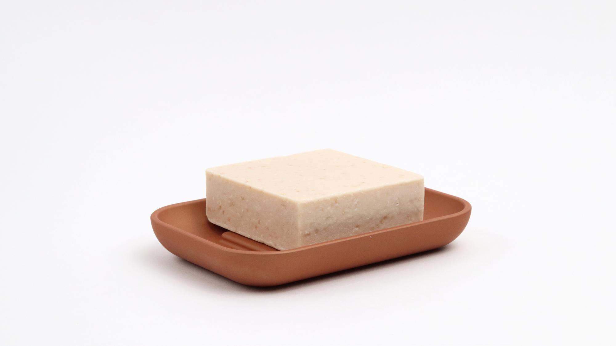 A terra cotta soap dish by Rous Hardware with a natural soap inside of the dish. 