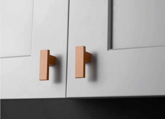Close-up of white kitchen cabinet doors featuring copper l-bar knob, highlighting the warmth and elegance of copper hardware.