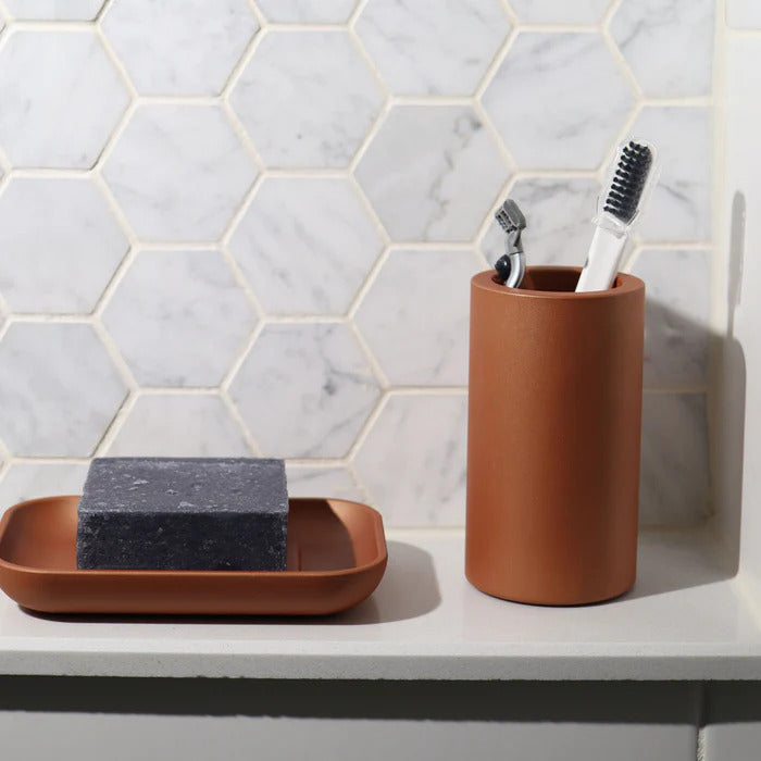 Terracotta cup and soap dish with black soap add a warm, modern touch to bathroom decor against a hexagonal marble tile wall.