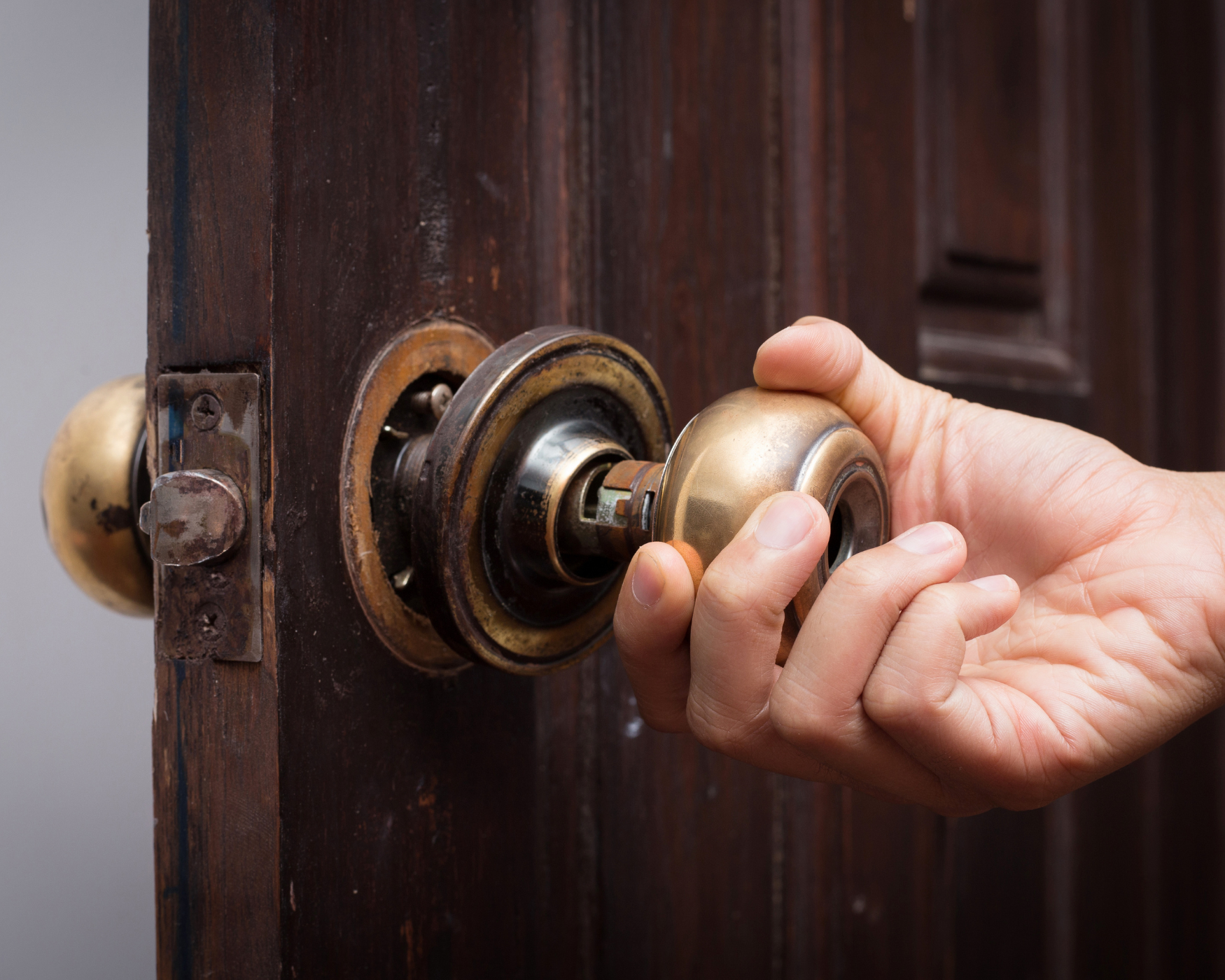 Close-up of a hand turning an antique brass door knob, showcasing its functional and decorative role in home design.