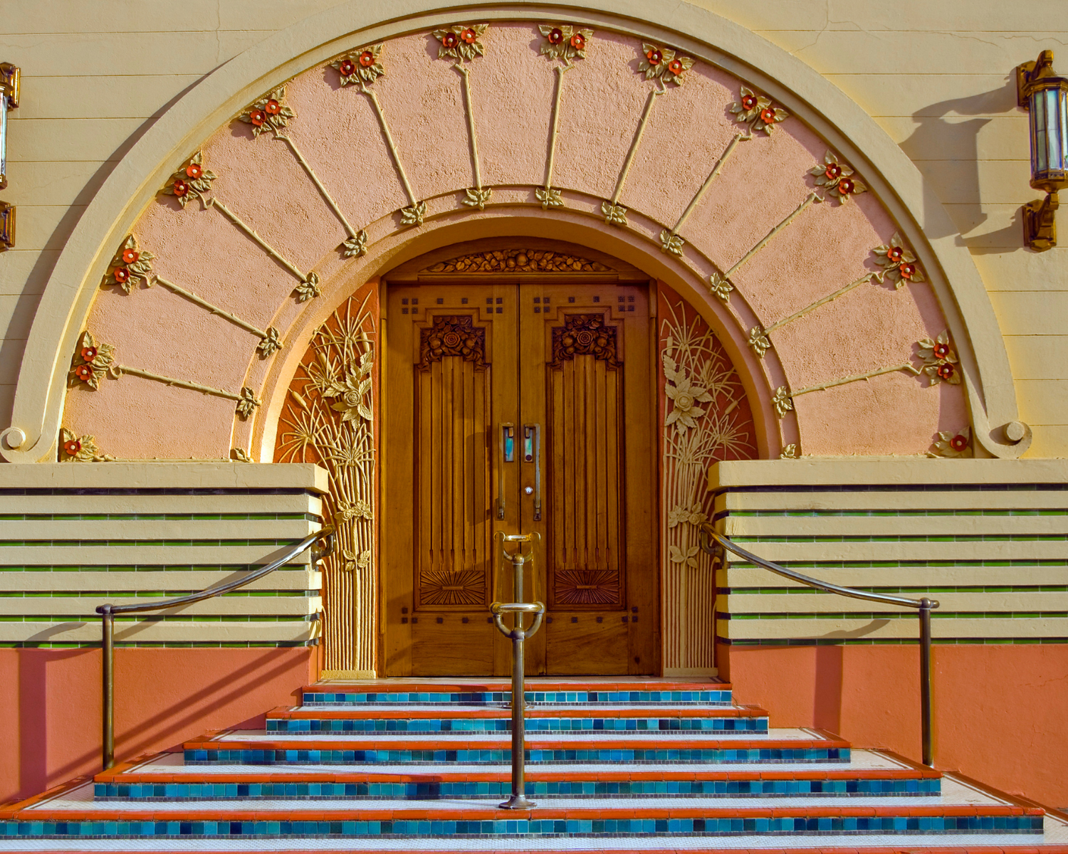 An Art Deco style doorway with a wooden entrance, floral arch, and vibrant blue tiled steps, reflecting luxurious design.