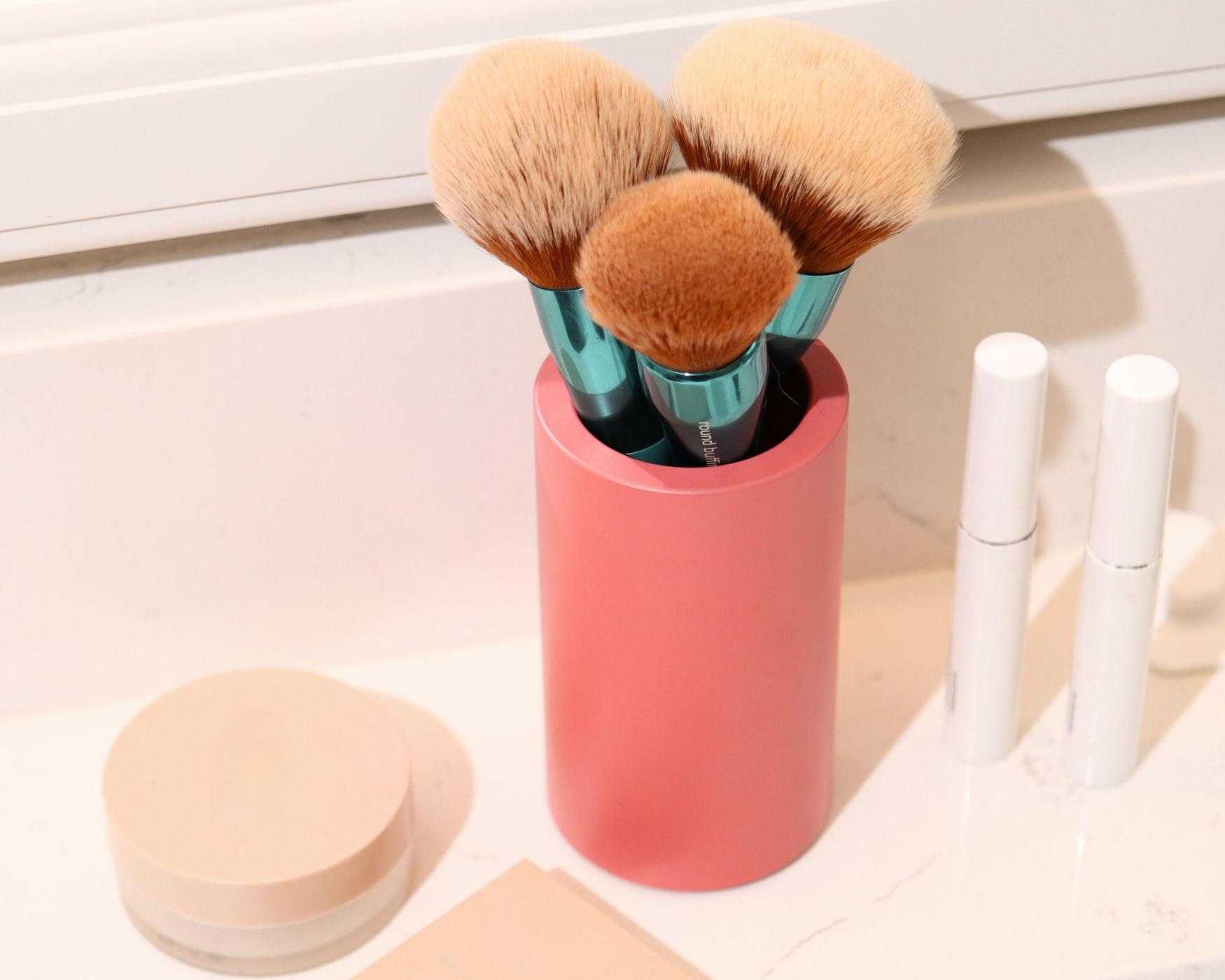 Pink vanity cup holding makeup brushes, offering a stylish and organized way to store essential beauty tools