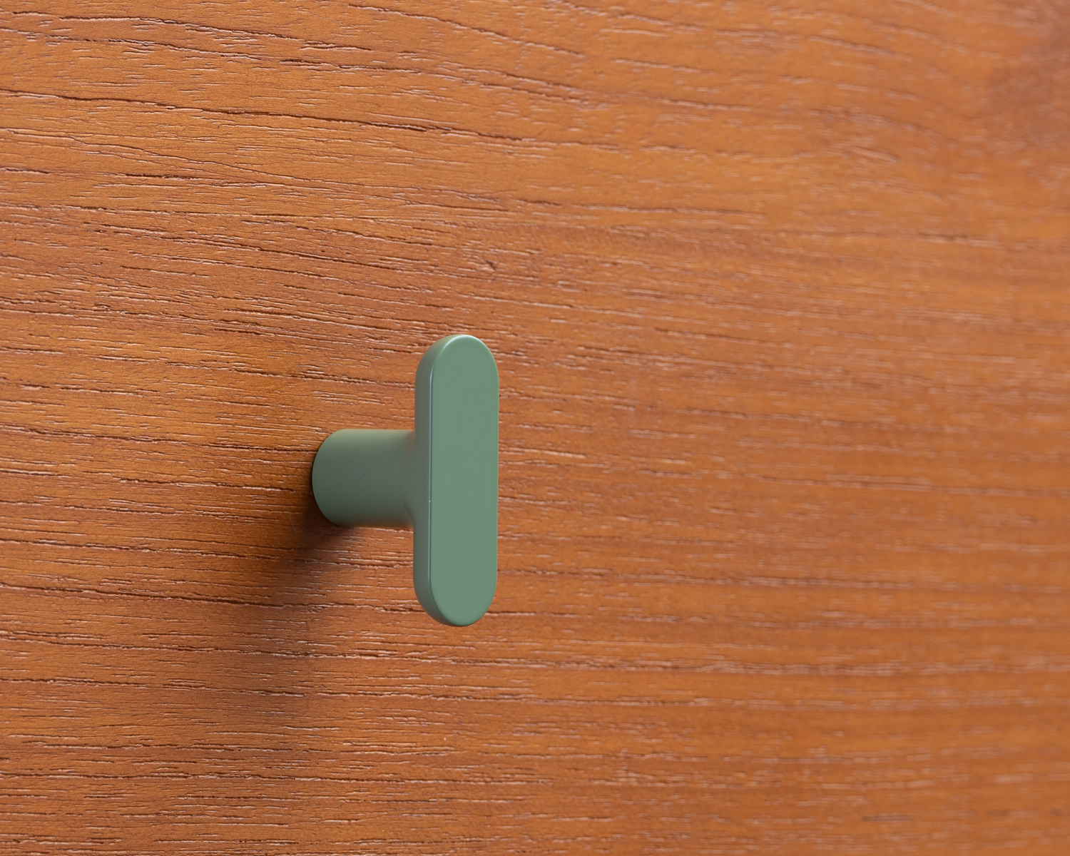 Olive green T-bar knob mounted on a wooden cabinet surface, from ROUS’s colorful hardware line for Mid Century Modern decor.