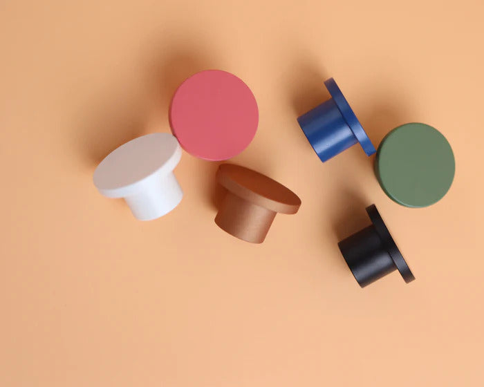 Assorted ROUS round knobs in rose, olive, copper, snow, navy, and charcoal on a peach background—simple yet striking.