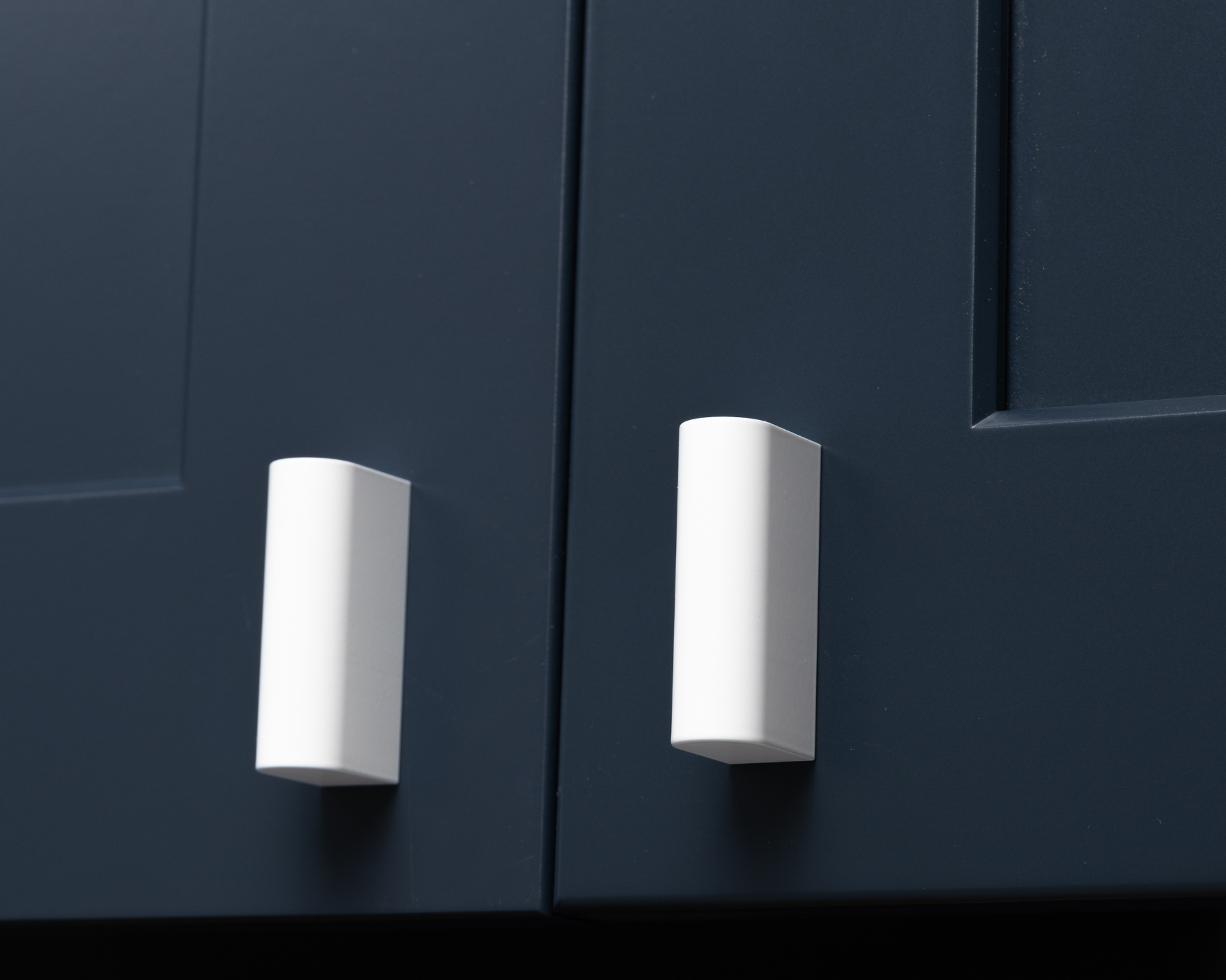 Close-up image of modern white cabinet knobs installed on a navy blue cabinet door, highlighting sleek, minimalist design.