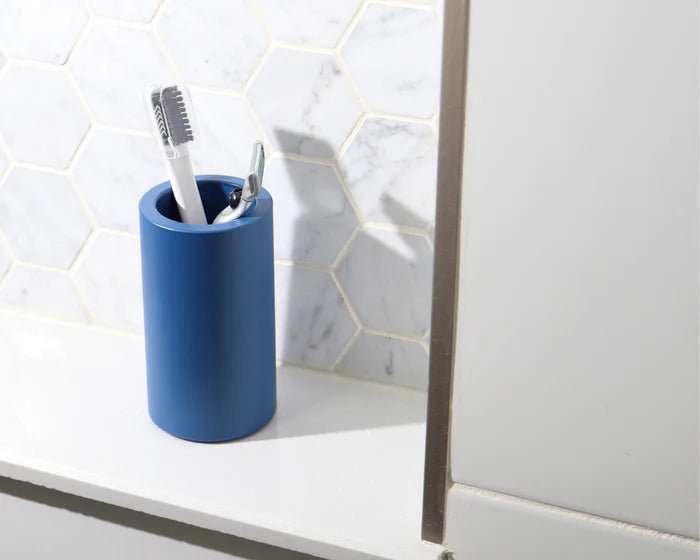 Blue vanity cup holding a toothbrush and razor on a white bathroom countertop with a hexagon tile backsplash
